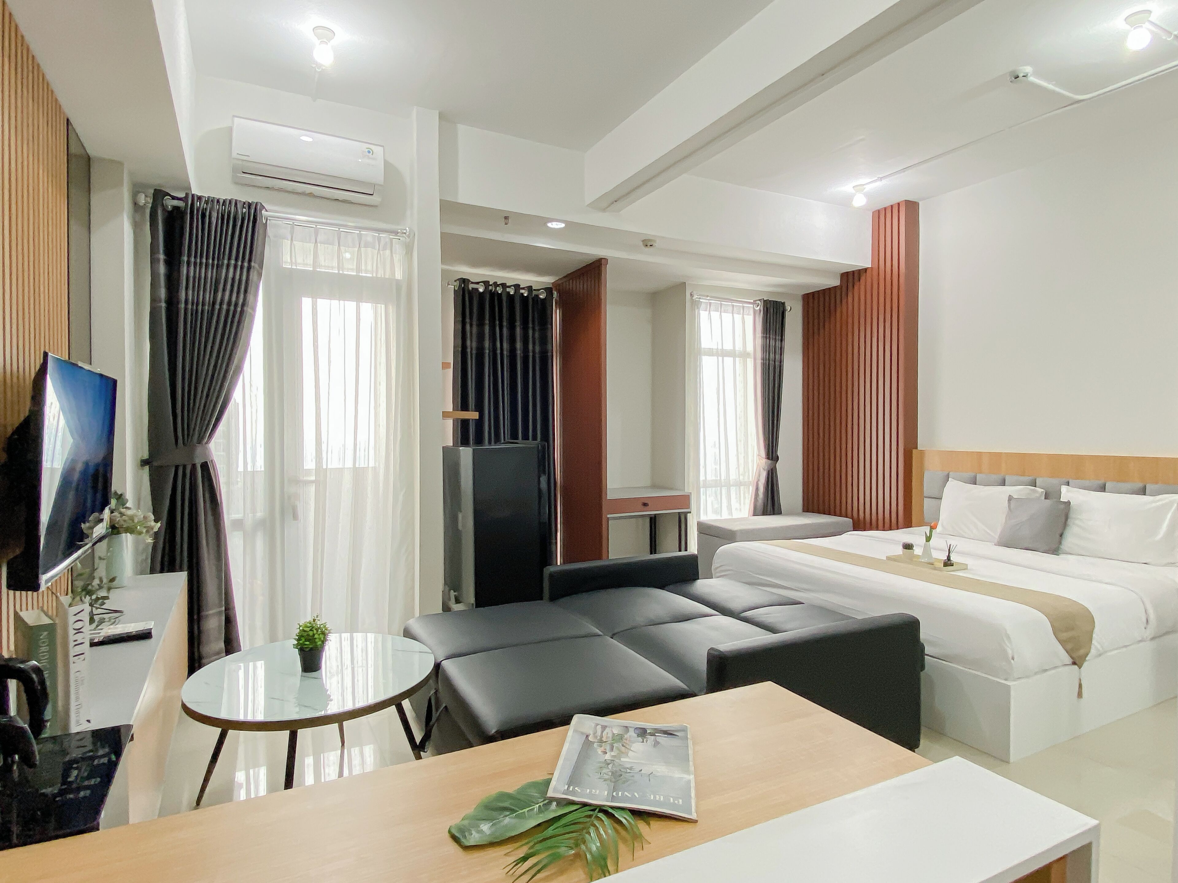 Una habitación de hotel moderna con cama, sofá, mesa de comedor y televisión.