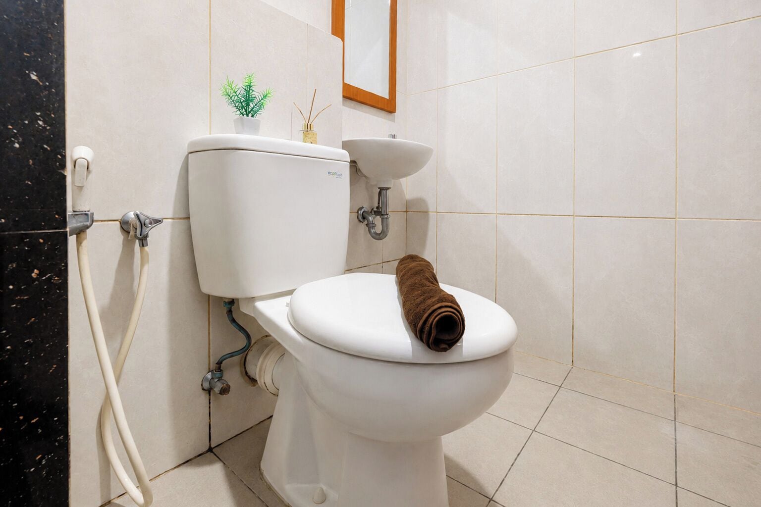A toilet with a towel on the seat, a small plant, and a picture frame on the wall.