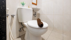 A toilet with a towel on the seat, a small plant, and a picture frame on the wall. - Comfortable 1Br Without Living Room At Grand Kamala Lagoon Apartment (Bekasi)