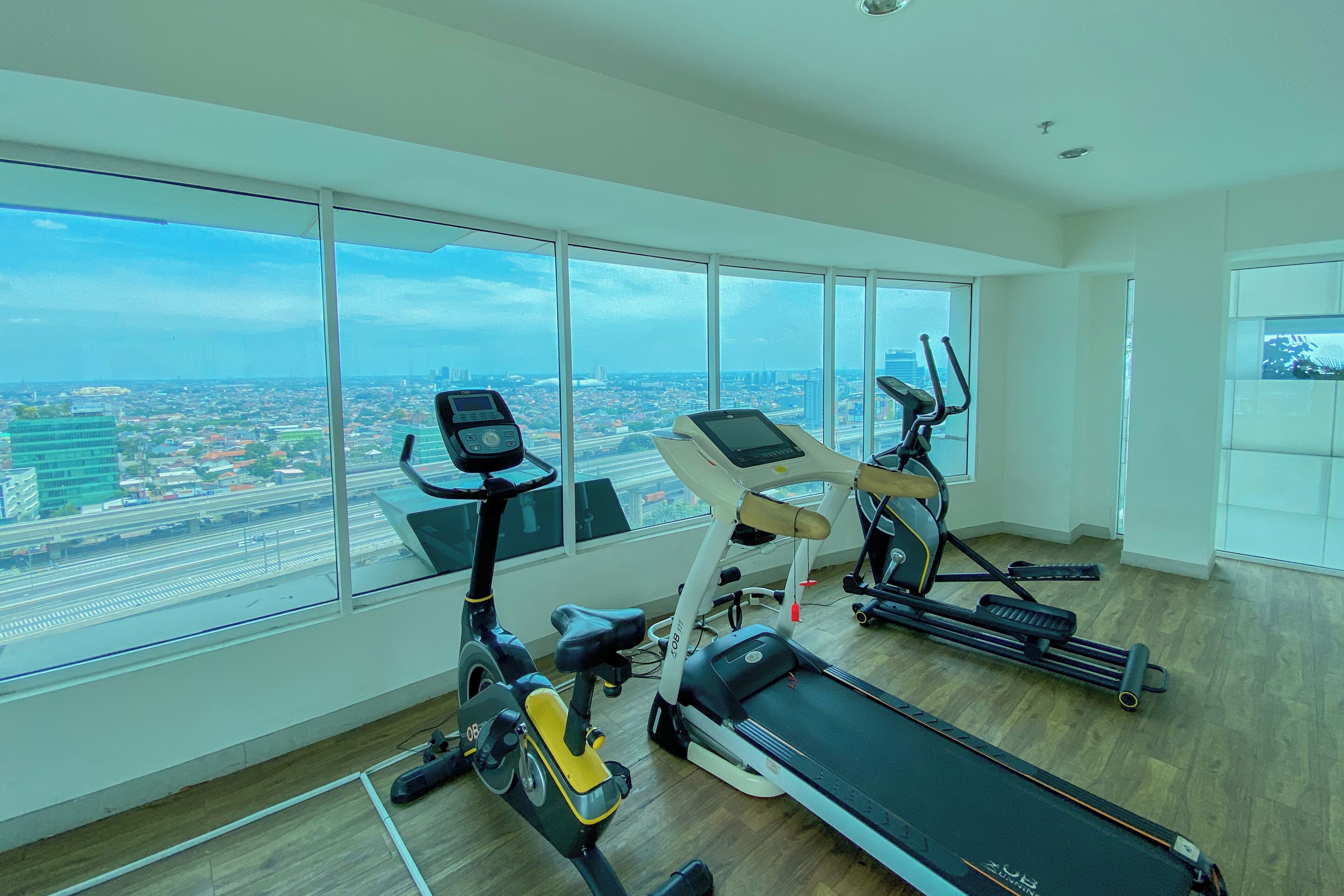 Un gimnasio con máquinas de cardio y un amplio ventanal con vista a la ciudad.
