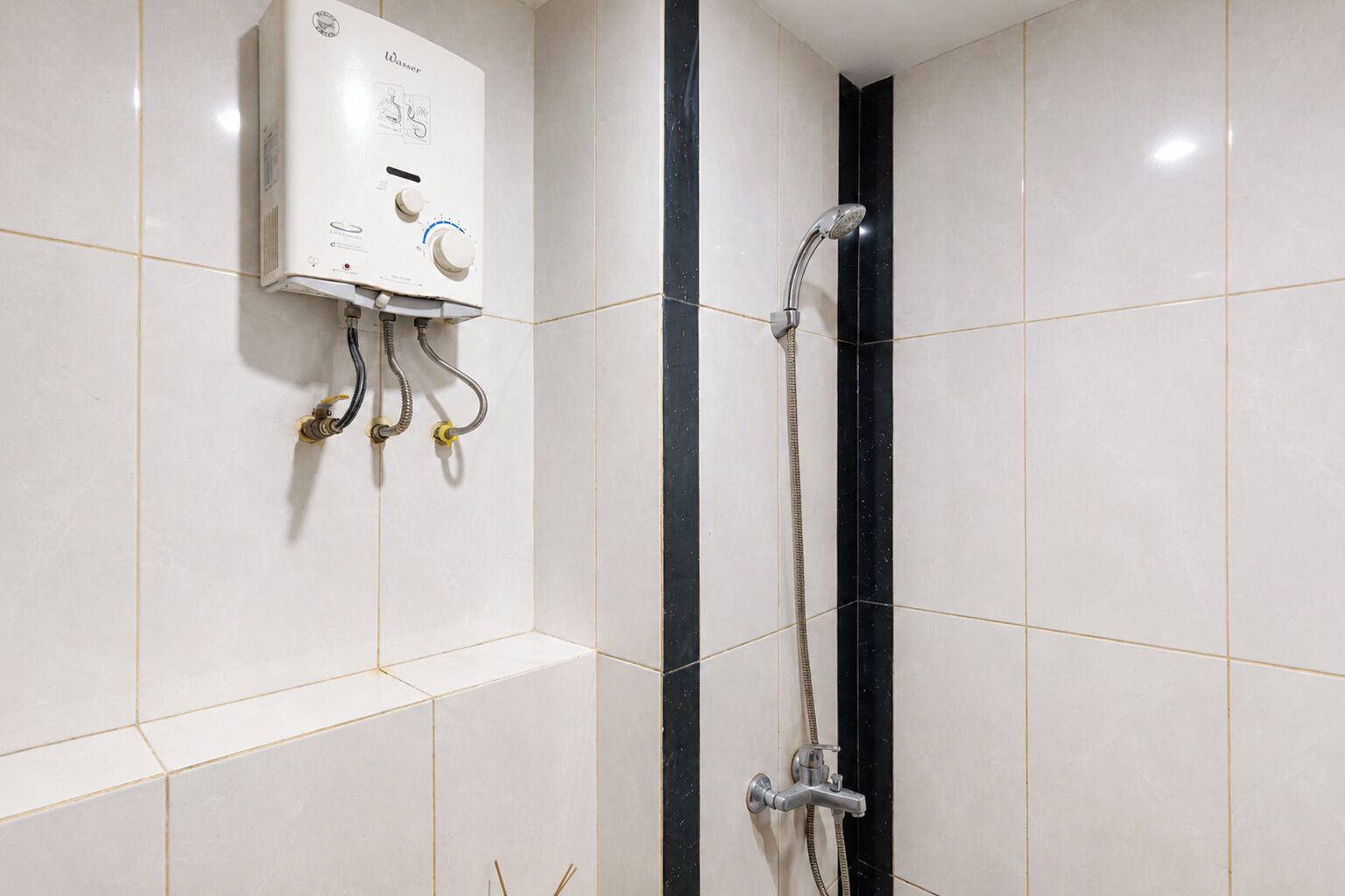 A bathroom with a white tiled wall, a water heater, and a shower with a black vertical stripe.