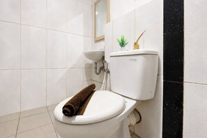 A bathroom with a white toilet, a sink, and a mirror. - Compact Style 1Br Without Living Room At Grand Kamala Lagoon Apartment (Bekasi)
