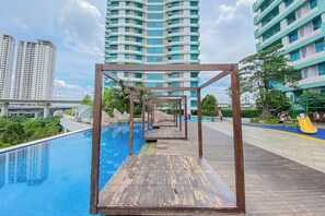 A swimming pool with wooden deck and a playground with slides. - Compact Style 1Br Without Living Room At Grand Kamala Lagoon Apartment (Bekasi)