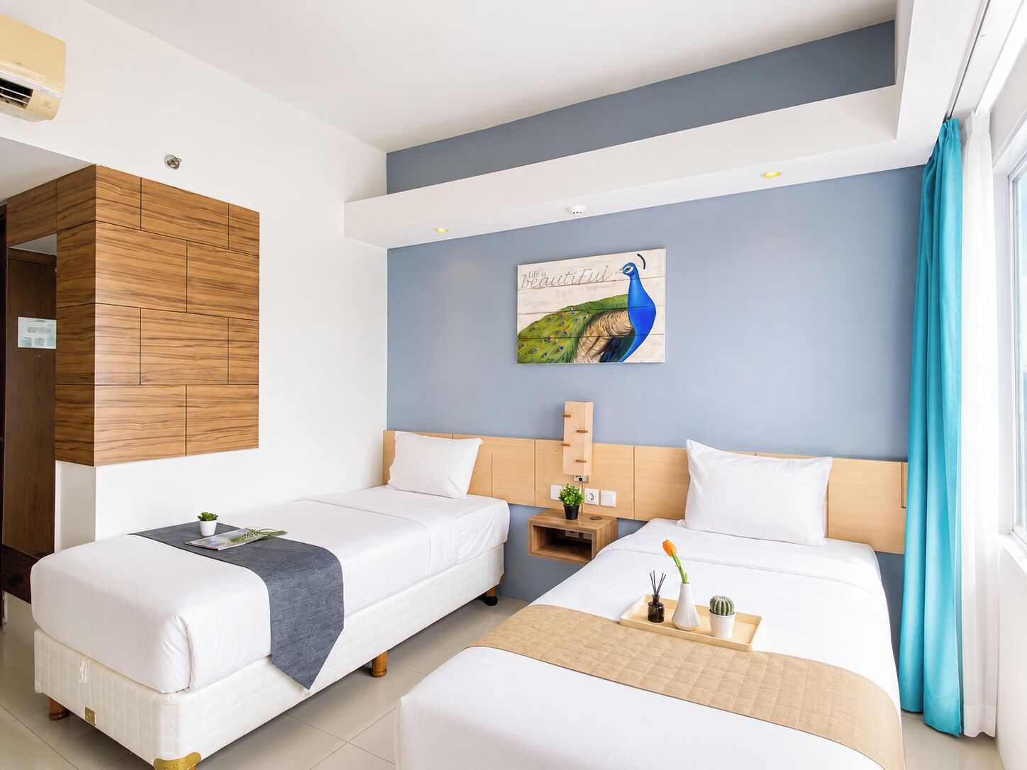 A hotel room with two beds, a wooden wardrobe, a wall-mounted artwork, and a window with curtains.