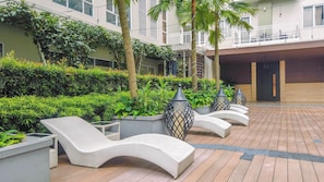 Un patio con sillas de descanso, plantas en macetas y un edificio con balcones.