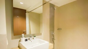 Un bagno con un lavandino bianco, uno specchio, una doccia e una porta in legno.