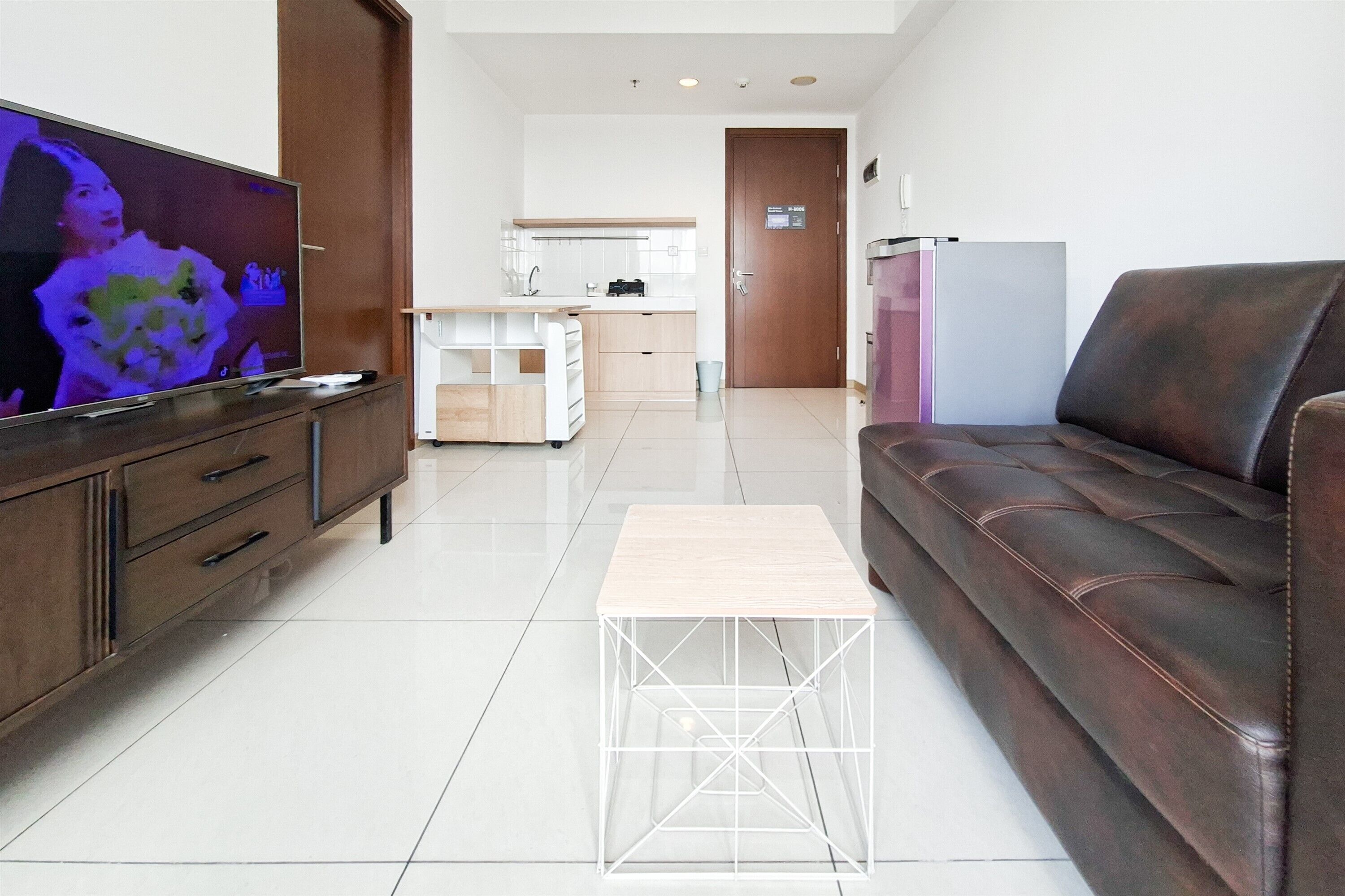 Un salon moderne avec une télévision, un canapé, une table basse et un coin cuisine à l’arrière-plan.