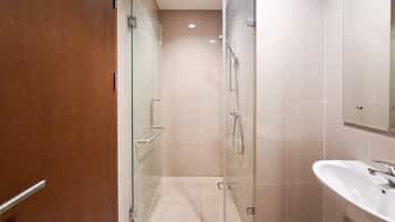 Een moderne badkamer met een douchecabine van glas, een witte wastafel en een houten deur.