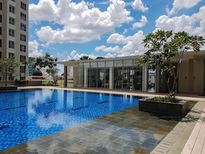 Uma piscina com superfície de água azul cristalina, rodeada por um deck ladrilhado.
