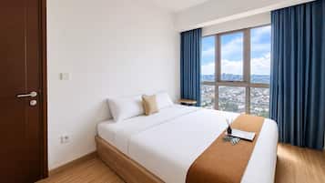 A hotel room with a bed, a window with curtains, a view of a cityscape, and a wooden floor.