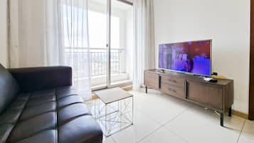 A living room with a leather sofa, a television on a wooden stand, and a balcony with a view of the city.