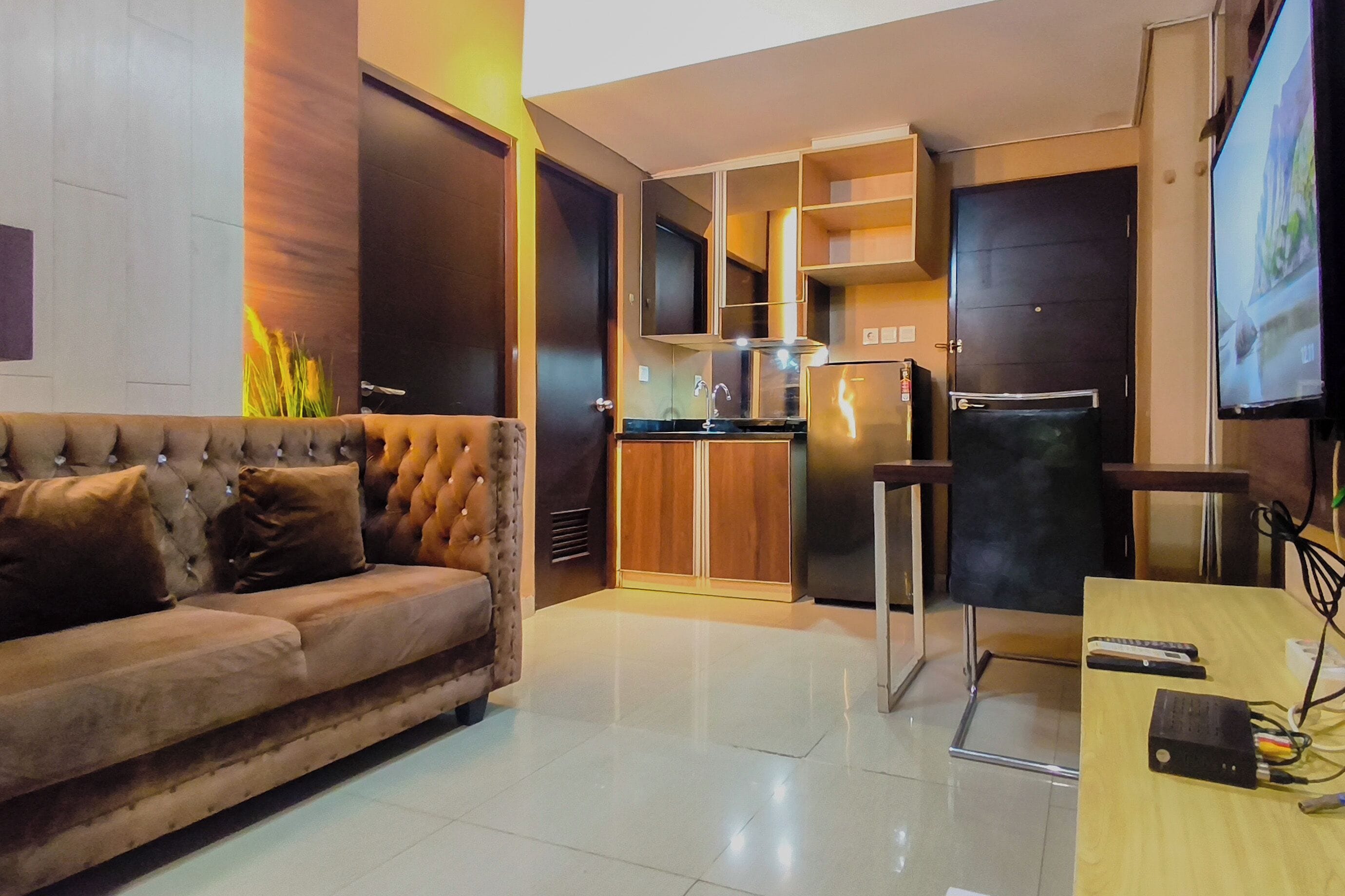A modern living room with a sofa, a kitchen area with a refrigerator, and a television.