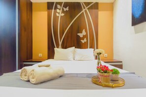A hotel room with a neatly made bed, a bedside table with a remote control, and a tray with flowers and a basket. - Well Furnished 2Br At Apartment Tamansari Papilio (Surabaya)