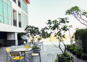 An outdoor seating area with tables and chairs, surrounded by potted plants and a view of a building. - Well Furnished 2Br At Apartment Tamansari Papilio (Surabaya)