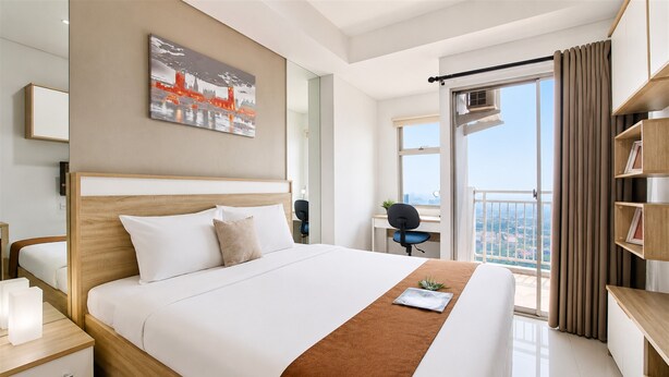 Een moderne hotelkamer met een groot bed, een bureau, een stoel, een boekenkast en uitzicht op een stadsgezicht.