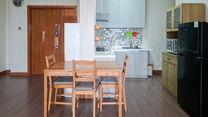 A compact kitchen with a dining area, a refrigerator, and a wooden door. - Comfortable 3Br Apartment At Great Western (Tangerang)