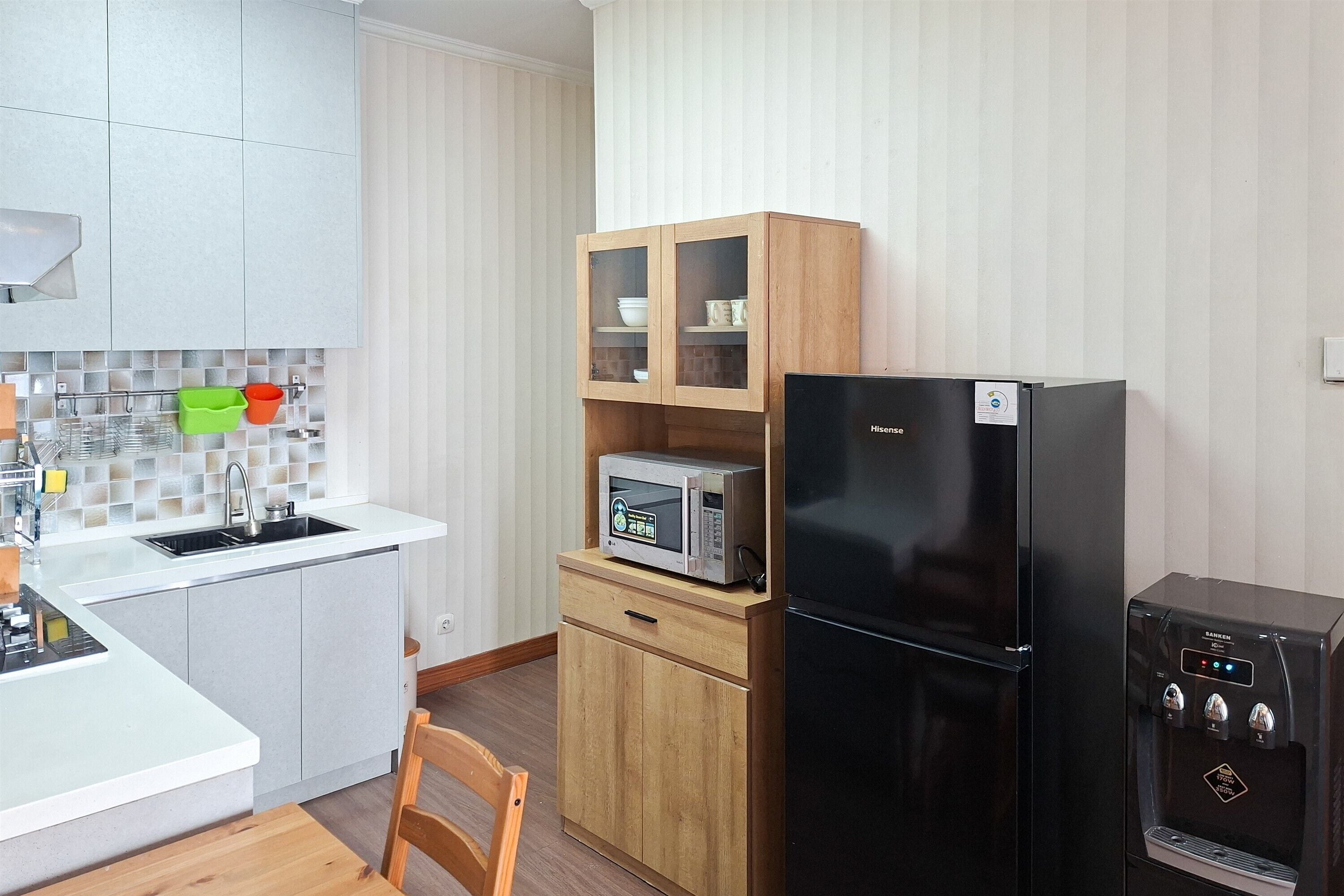 A compact kitchen with a sink, a microwave, a refrigerator, and a cabinet with glass doors.
