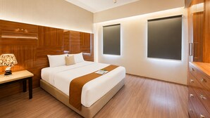 A hotel room with a large bed, wooden headboard, bedside table with lamp, and a wardrobe. - Comfortable 3Br Apartment At Great Western (Tangerang)