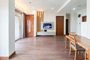 A spacious living area with a wooden dining table and chairs, a flat-screen TV mounted on a wall, and a sliding door leading to another room. - Comfortable 3Br Apartment At Great Western (Tangerang)