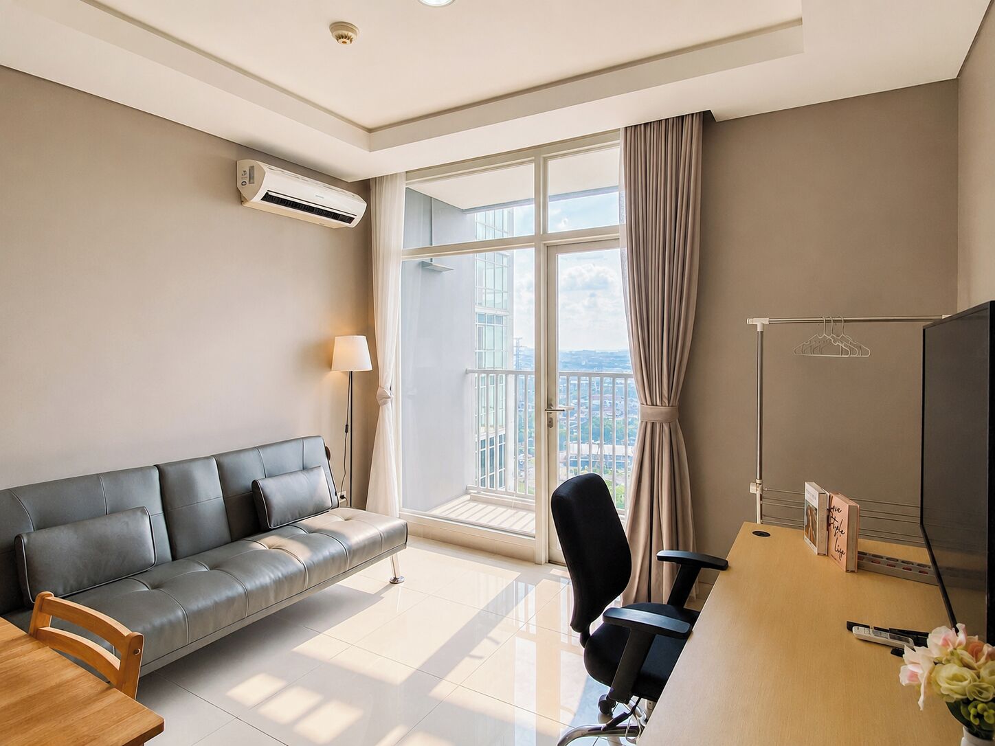 A modern hotel room with a leather sofa, a desk with a chair, a large window with curtains, and a flat-screen TV.