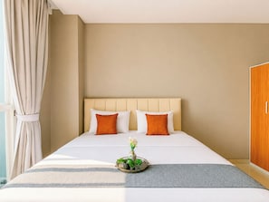 Een hotelkamer met een bed, twee kussens, een nachtkastje met een bloemetje en een kledingkast.