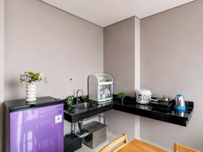 Een kleine keuken met een geïntegreerde koelkast, een koffiezetapparaat, een waterkoker en een fornuis.