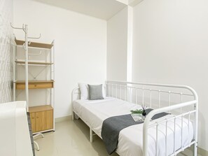 A small, white, single-bed room with a metal bed frame, a wooden shelf unit, and a white wardrobe. - Comfortable 2Br At Apartment Signature Park Grande (Jakarta)