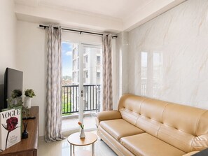 A modern living room with a leather sofa, a small round table with a vase, and a TV on a stand. - Comfortable 2Br At Apartment Signature Park Grande (Jakarta)