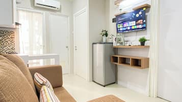 Una sala moderna con un sofá, un televisor de pantalla plana montado en la pared, un refrigerador y un pequeño estante con objetos decorativos.