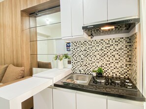 A modern kitchen with a black countertop, stainless steel sink, and a gas stove. - Nice Homey 2Br At Apartment Green Pramuka City (Jakarta)