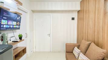 Una sala de estar con un televisor de pantalla plana montado en la pared, un sofá con cojines a rayas y un mueble de madera con una planta en maceta.