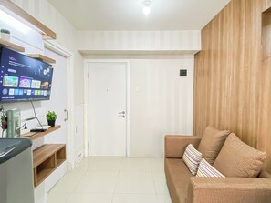 A living room with a flat-screen TV mounted on the wall, a sofa with striped cushions, and a wooden cabinet with a potted plant. - Nice Homey 2Br At Apartment Green Pramuka City (Jakarta)