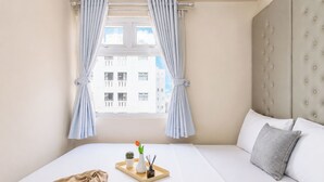 Una camera d'albergo con un letto, una finestra con tende e una vista sui palazzi, più un comodino con un vassoio.