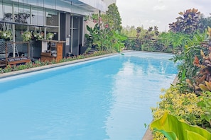 Ein Swimmingpool mit einem Schild für einen Essensstand, umgeben von üppiger Vegetation und einem modernen Gebäude im Hintergrund.