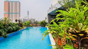 A swimming pool surrounded by lush greenery and modern buildings in the background. - Bright And Convenient 2Br At Apartment Tuscany Residence (Tangerang)