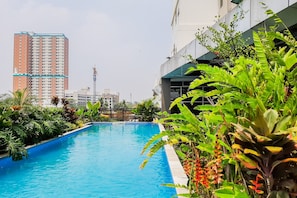 Ein Swimmingpool, umgeben von üppiger Vegetation und modernen Gebäuden im Hintergrund.
