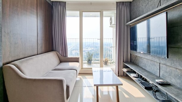A modern living room with a sofa, a flat-screen TV, a small table, and a balcony with a view. - Bright And Convenient 2Br At Apartment Tuscany Residence (Tangerang)