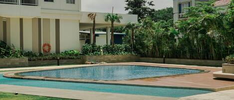 A swimming pool with a surrounding deck, a lifebuoy, and a building with balconies and windows.
