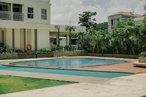 Una piscina con un deck perimetral, un flotador salvavidas y un edificio con balcones y ventanas.