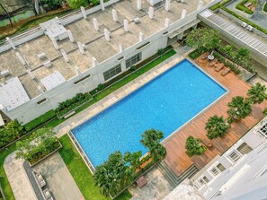 Vista aérea de un edificio moderno con piscina rectangular rodeada por una terraza de madera y follaje.