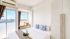 Et hotelværelse med seng, natbord, et vindue med gardiner og udsigt over byen.