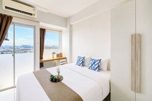 Habitación de hotel con cama, mesita de noche, ventana con cortinas y vista a la ciudad.
