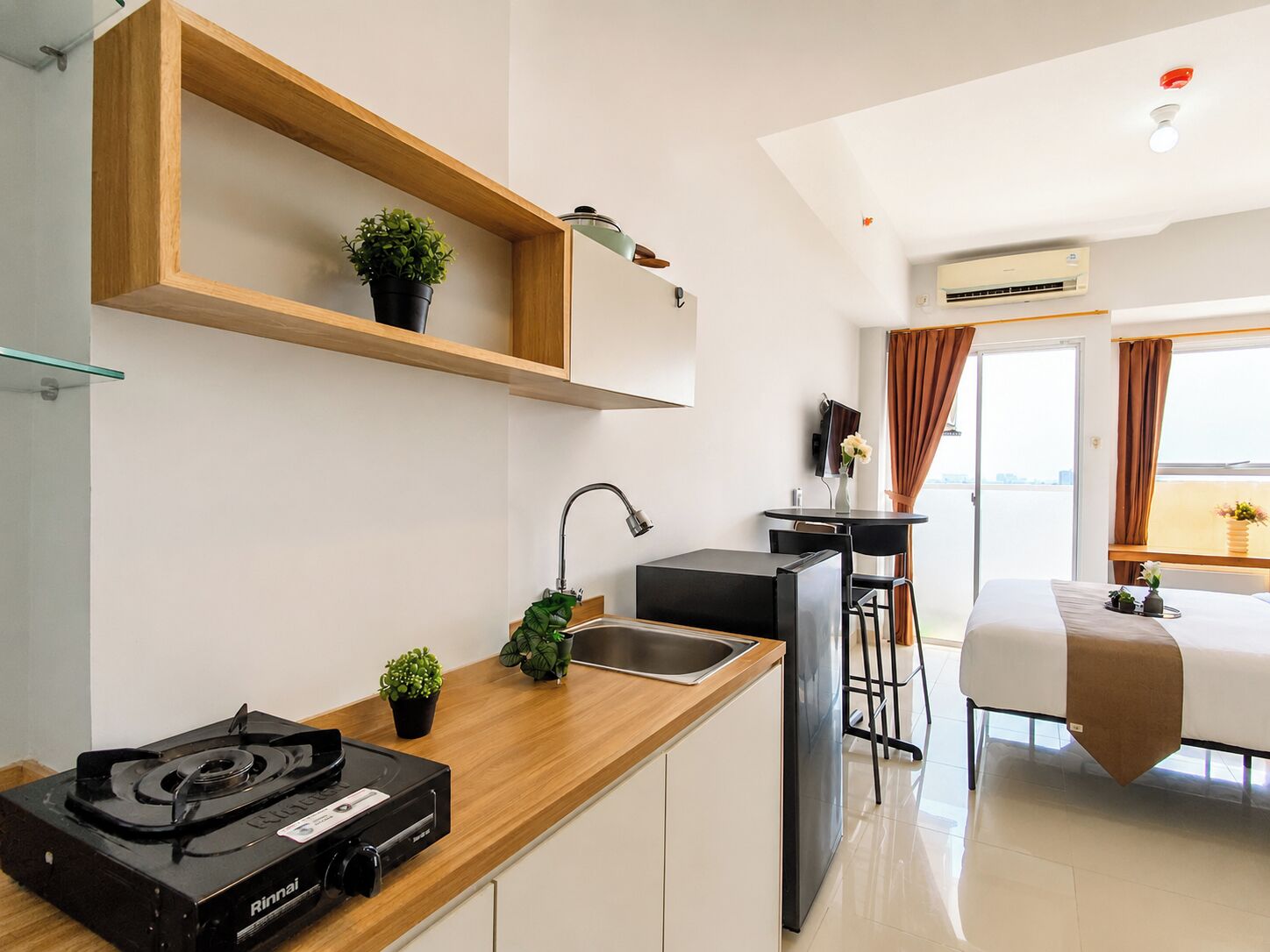 Quarto de hotel moderno com cozinha compacta, cama, área de refeições e vista para a cidade.