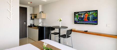 Een hotelkamer met een bed, een eettafeltje, een aan de muur bevestigde televisie en een kitchenette op de achtergrond.