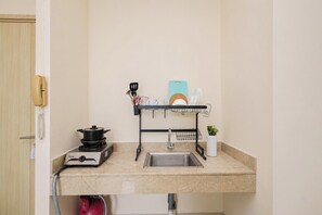 A compact kitchenette with a stove, sink, and a drying rack for dishes. - Bright Minimalist 2Br At Apartment Elpis Residence (Jakarta)