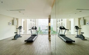 A gym with treadmills and stationary bikes, large windows, and a view of buildings. - Bright Minimalist 2Br At Apartment Elpis Residence (Jakarta)