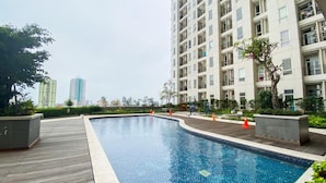 A swimming pool with a wooden deck, surrounded by residential buildings and greenery. - Bright Minimalist 2Br At Apartment Elpis Residence (Jakarta)