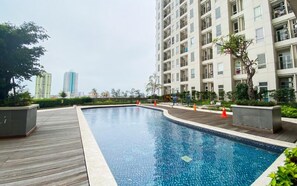 A swimming pool with a wooden deck, surrounded by residential buildings and greenery. - Bright Minimalist 2Br At Apartment Elpis Residence (Jakarta)