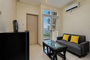 A modern living room with a sofa, a glass-top coffee table, and a bookshelf with books. - Bright Minimalist 2Br At Apartment Elpis Residence (Jakarta)