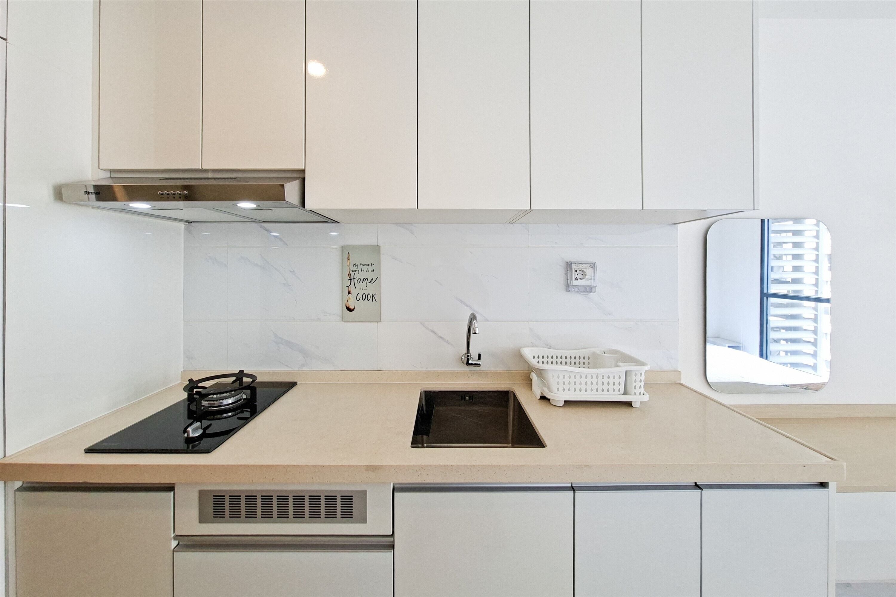Una cocina moderna con estufa a gas, campana extractora de acero inoxidable, gabinetes blancos, salpicadero de mármol y una ventana con vista a edificios.